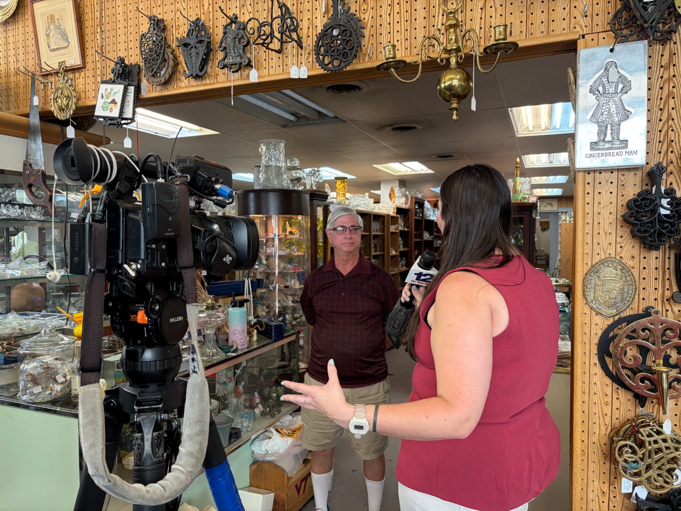 Amory Doyle interviewing a man in an antique store with a 12 On Your Side microphone while a news camera records