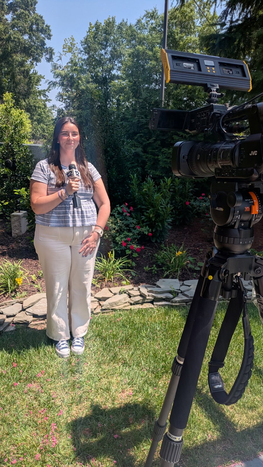 Amory Doyle holding a 12 On Your Side microphone beside a video camera on a tripod