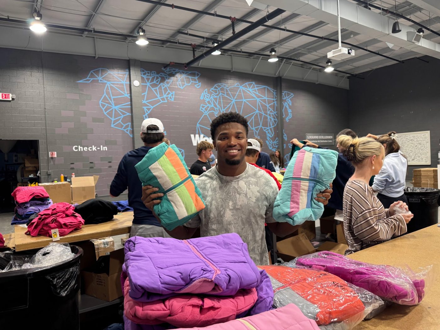 A volunteer smiling and holding up two folded coats at a humanitarian aid distribution center