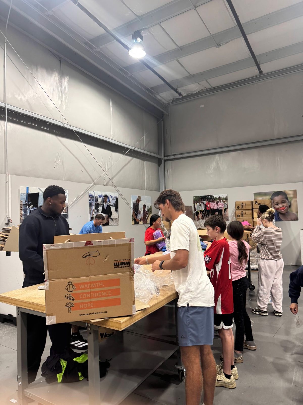Volunteers sorting and packing clothing at long work tables in a warehouse